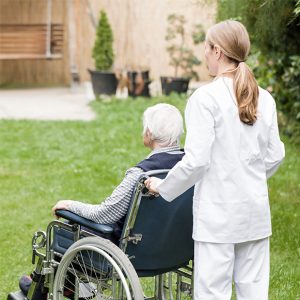 Foto på en kvinna i vårdkläder som kör en äldre man i rullstol. Bilden symboliserar LONE-studien och resultatet från den som visar att existentiell ensamhet bland äldre är en utmaning för vården.