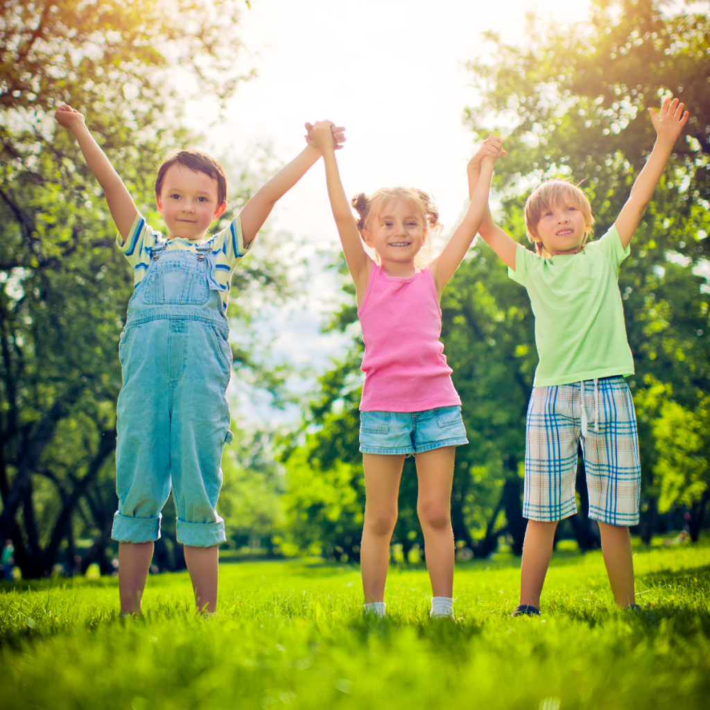Tre barn som hoppar i gräset en sommardag.