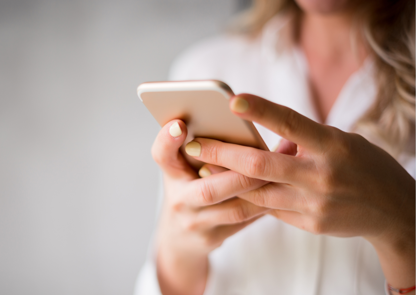 Närbild på en person i vit skjorta som håller en mobiltelefon i båda händerna.