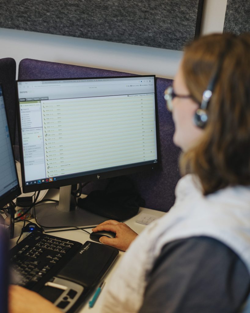 En sjuksköterska på Bräcke vårdcentral Centralhälsan sitter med hörlurar vid ett skrivbord med datorskärmar