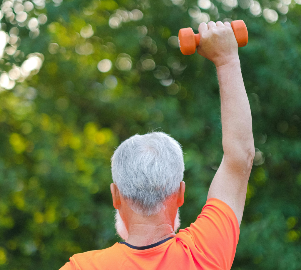 En man håller upp en hantel som är orange, man ser honom bakifrån och han har en orange tröja på sig. Han rehabiliterar