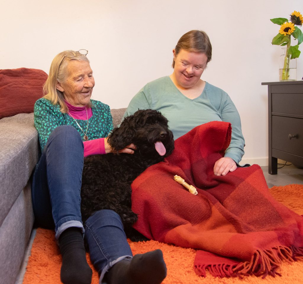 En äldre mamma och hennes medelålders dotter tillsammans med en svart hund (cockerpoo)